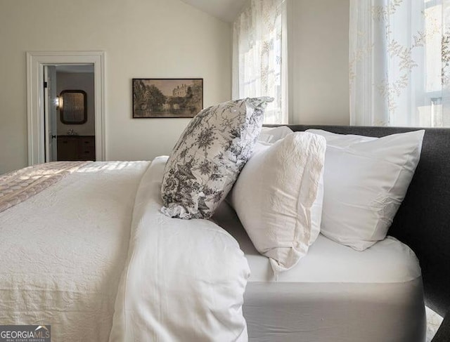 bedroom with ensuite bathroom, multiple windows, and vaulted ceiling