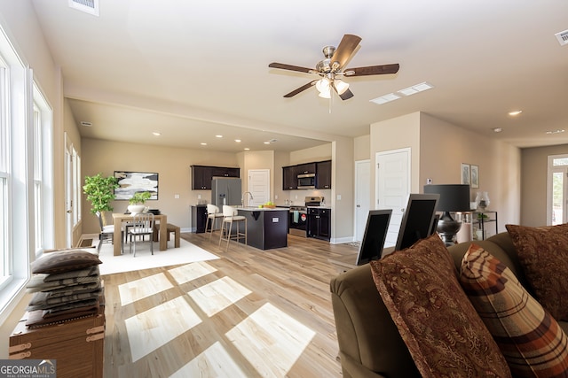 living room with light wood-type flooring, sink, and ceiling fan