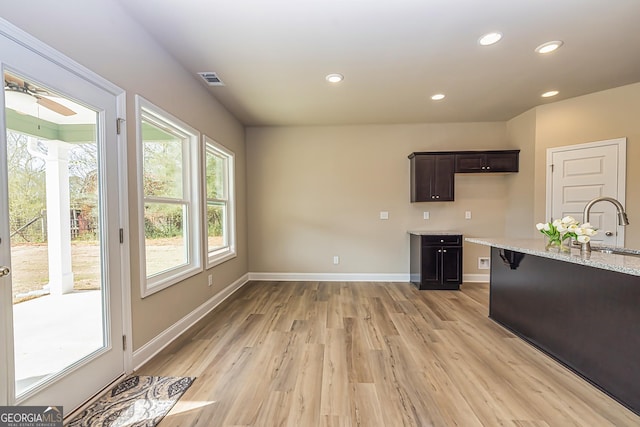 kitchen featuring sink, dark brown cabinets, light stone counters, and light hardwood / wood-style flooring