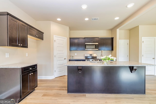 kitchen with a center island with sink, stainless steel appliances, and light stone counters