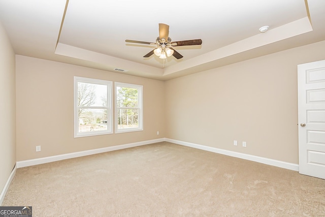 carpeted empty room with a raised ceiling and ceiling fan