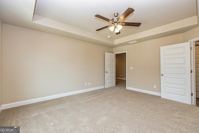 carpeted spare room with a tray ceiling and ceiling fan