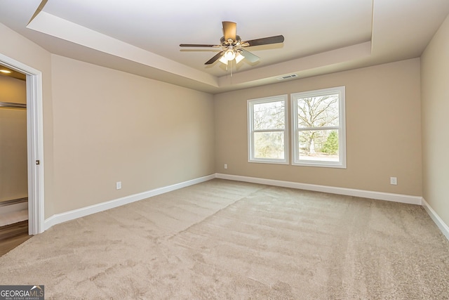 empty room with a tray ceiling, light carpet, and ceiling fan