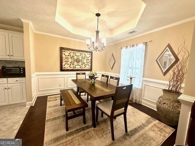 dining room with a tray ceiling, ornamental molding, a notable chandelier, and wood-type flooring