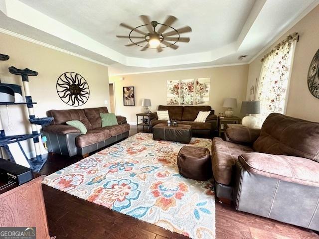 living room with hardwood / wood-style flooring, ceiling fan, and a raised ceiling