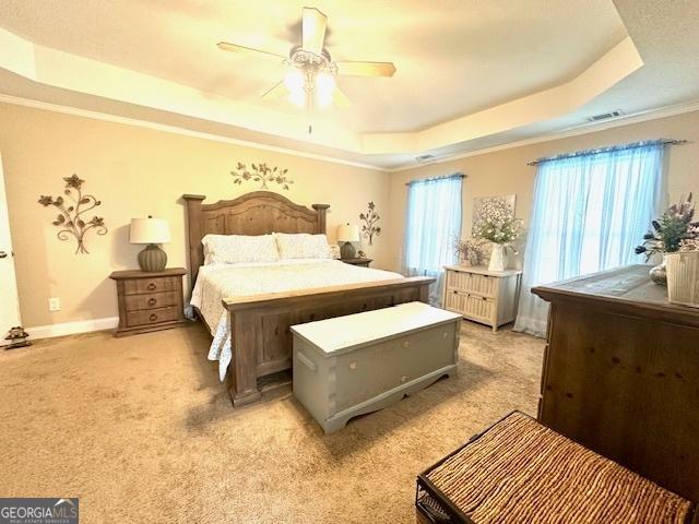 carpeted bedroom with a tray ceiling, crown molding, and ceiling fan