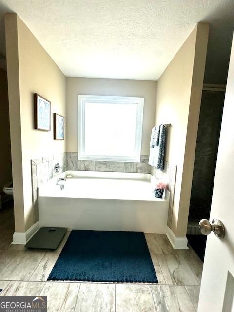 bathroom with a washtub, a textured ceiling, and toilet