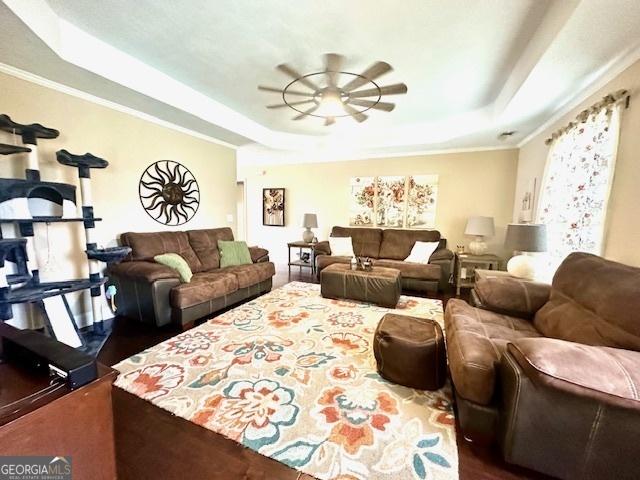 living room with a tray ceiling, ornamental molding, and ceiling fan