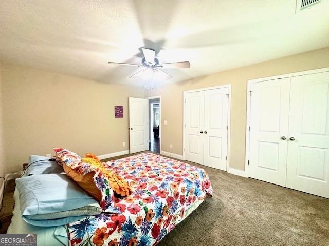 carpeted bedroom with ceiling fan and two closets