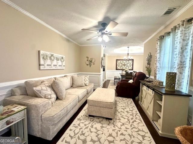 living room featuring ceiling fan with notable chandelier, ornamental molding, wood-type flooring, and a textured ceiling