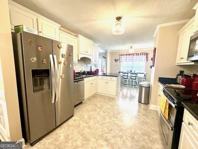 kitchen with appliances with stainless steel finishes, kitchen peninsula, crown molding, and white cabinets