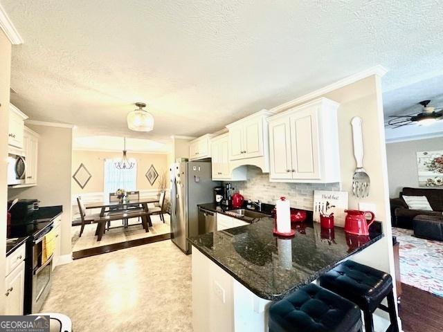 kitchen with appliances with stainless steel finishes, a kitchen breakfast bar, decorative light fixtures, kitchen peninsula, and white cabinets