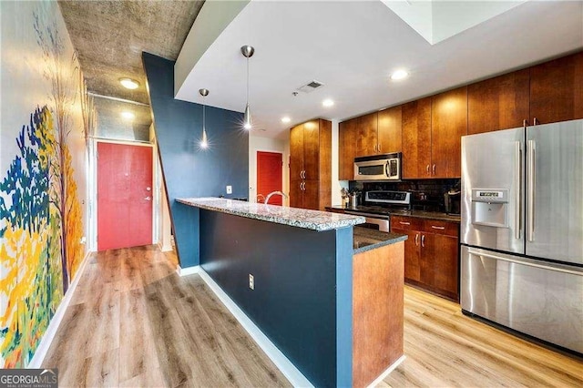 kitchen with a kitchen island with sink, light hardwood / wood-style flooring, tasteful backsplash, appliances with stainless steel finishes, and pendant lighting