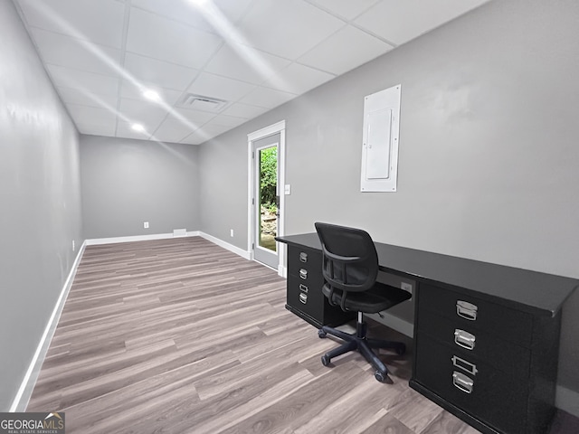 home office with electric panel, light hardwood / wood-style floors, and a paneled ceiling