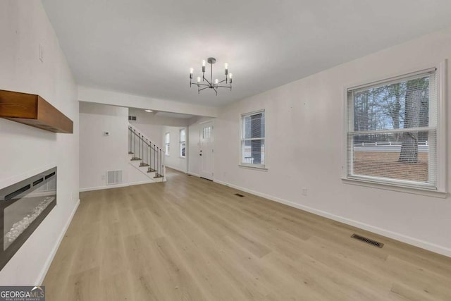 unfurnished living room featuring light wood-type flooring and a notable chandelier