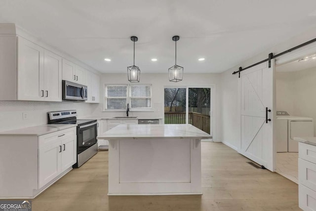 kitchen featuring white cabinets, appliances with stainless steel finishes, a barn door, and washing machine and dryer