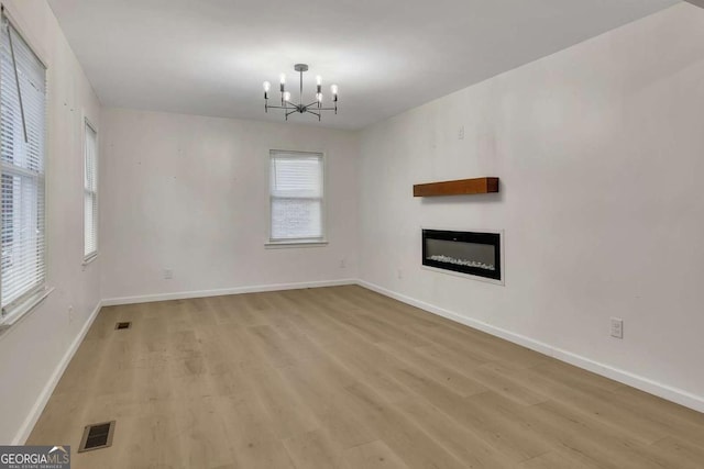 unfurnished living room featuring a wealth of natural light, light hardwood / wood-style floors, and a notable chandelier