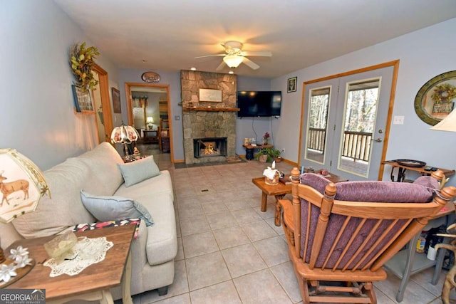 tiled living room featuring ceiling fan and a stone fireplace