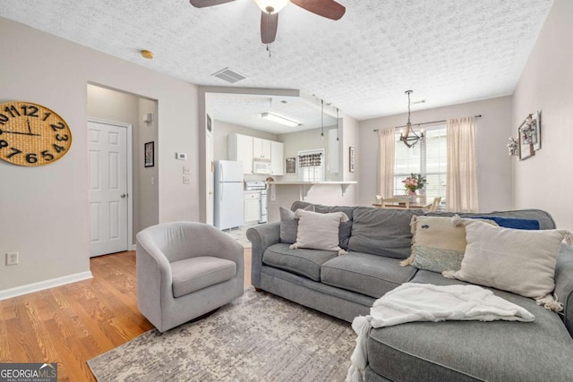 living room featuring a textured ceiling, light hardwood / wood-style floors, and ceiling fan with notable chandelier