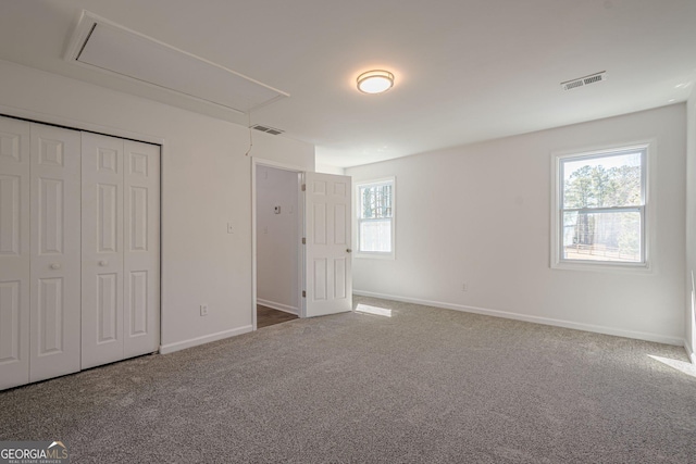 unfurnished bedroom featuring visible vents, baseboards, attic access, and carpet flooring