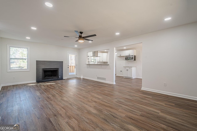 unfurnished living room with dark wood-type flooring, a fireplace with flush hearth, visible vents, and plenty of natural light