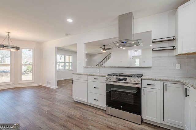 kitchen with stainless steel gas range, island exhaust hood, decorative backsplash, white cabinetry, and light wood-type flooring