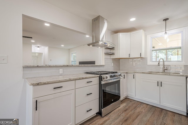 kitchen with tasteful backsplash, light wood finished floors, island exhaust hood, stainless steel gas range, and a sink