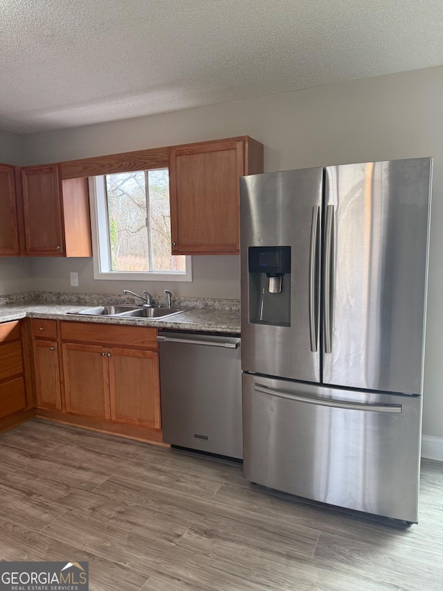 kitchen with light hardwood / wood-style flooring, stainless steel appliances, a textured ceiling, and sink