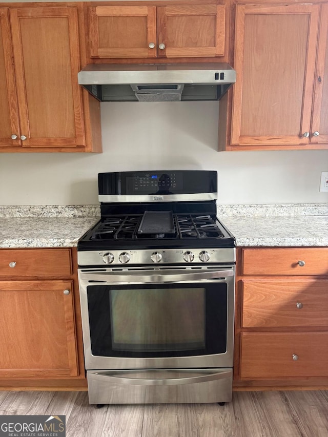 kitchen featuring light wood-type flooring, stainless steel gas stove, and light stone counters