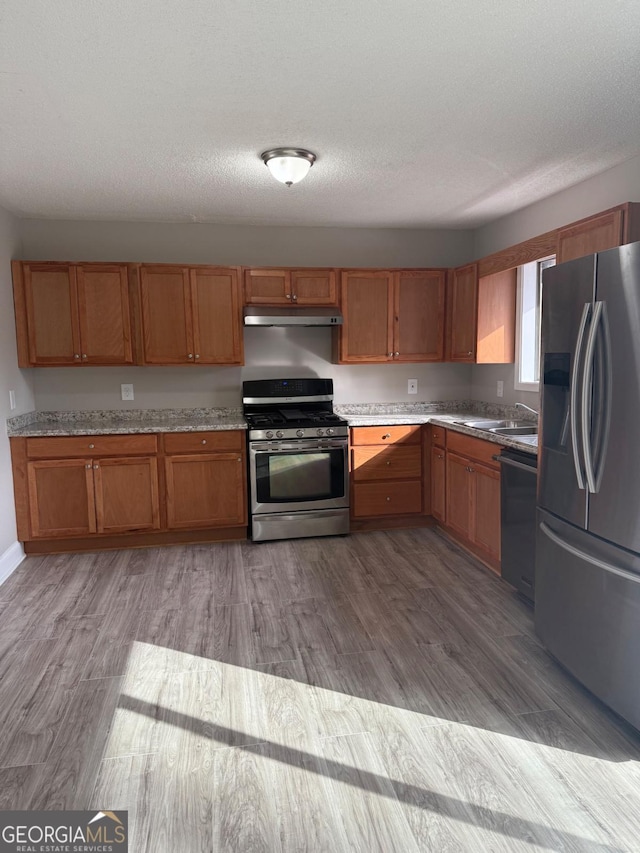 kitchen featuring appliances with stainless steel finishes, light hardwood / wood-style flooring, sink, and a textured ceiling