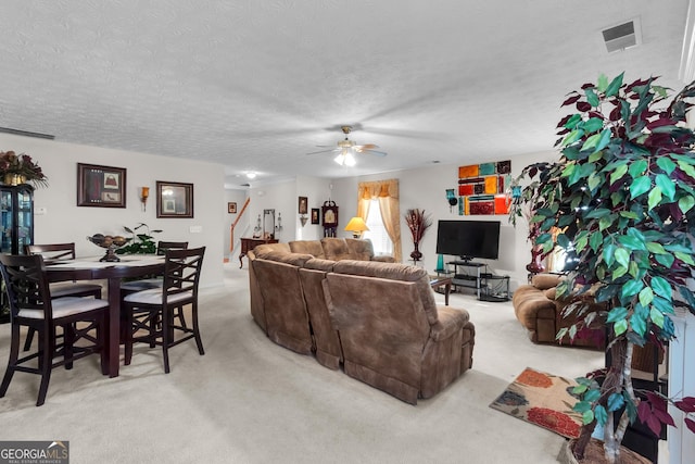 living room featuring visible vents, light colored carpet, stairway, ceiling fan, and a textured ceiling