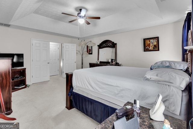 bedroom with visible vents, a tray ceiling, a ceiling fan, and light colored carpet