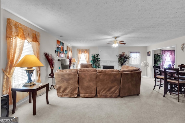 living room with ceiling fan, a fireplace, a textured ceiling, and light colored carpet