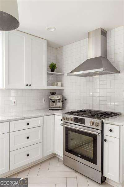 kitchen featuring backsplash, white cabinetry, wall chimney range hood, and stainless steel range with gas cooktop