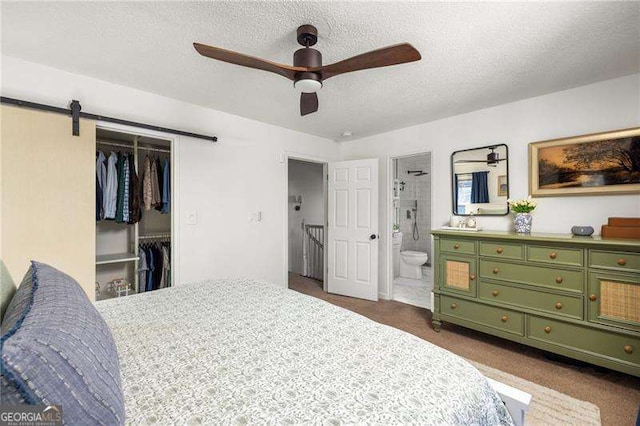 carpeted bedroom with a closet, a textured ceiling, ceiling fan, connected bathroom, and a barn door