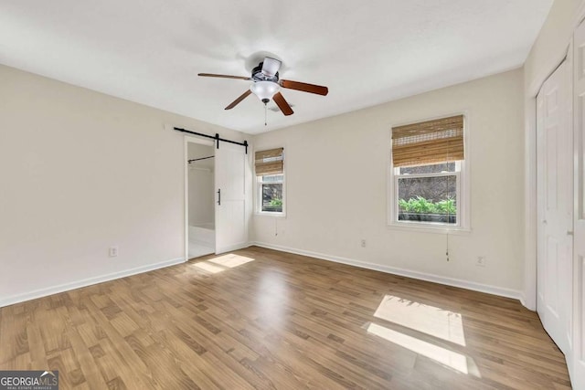 unfurnished bedroom featuring light hardwood / wood-style floors, a closet, ceiling fan, and a barn door