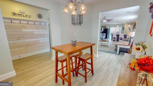 dining area with ceiling fan with notable chandelier and light hardwood / wood-style floors