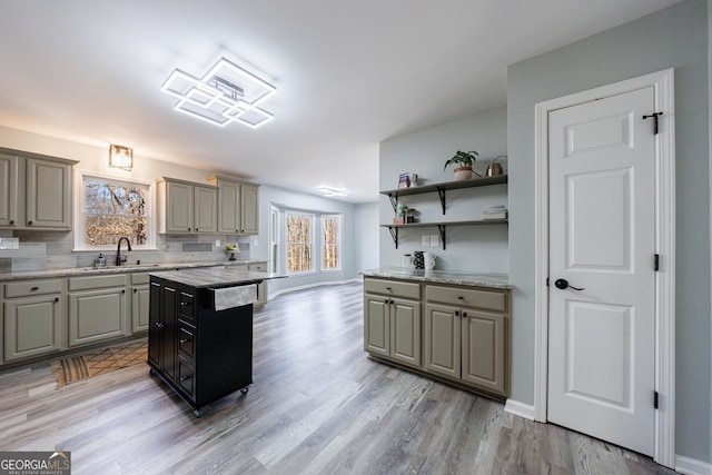 kitchen with open shelves, tasteful backsplash, gray cabinetry, a sink, and light wood-type flooring