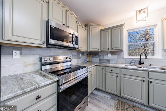 kitchen featuring appliances with stainless steel finishes, a sink, light stone countertops, gray cabinets, and backsplash