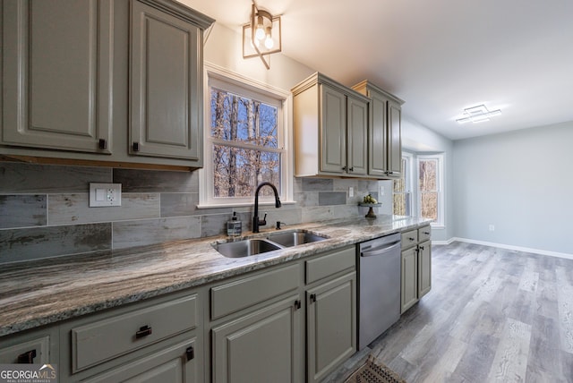 kitchen with light wood-style flooring, gray cabinetry, backsplash, stainless steel dishwasher, and a sink