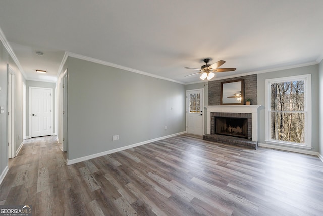 unfurnished living room featuring ornamental molding, a brick fireplace, wood finished floors, and baseboards