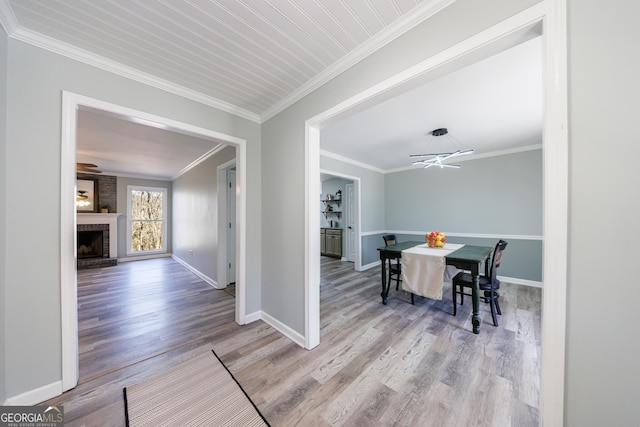 dining area featuring a brick fireplace, baseboards, ornamental molding, and wood finished floors