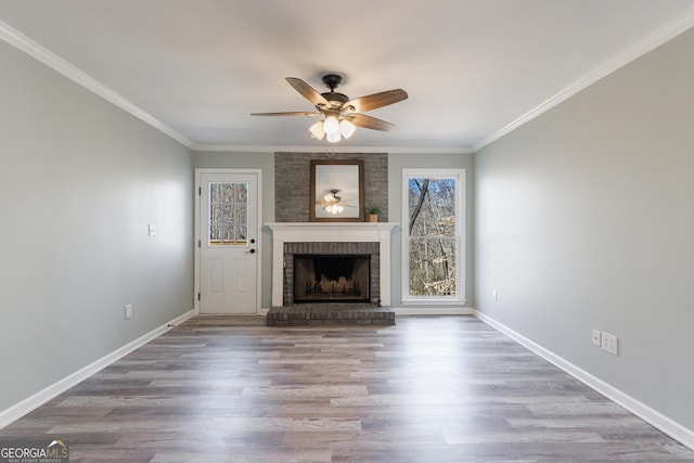 unfurnished living room featuring ornamental molding, a brick fireplace, wood finished floors, and baseboards