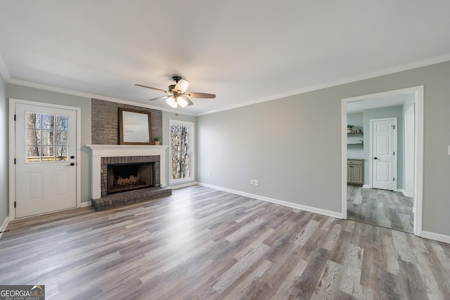 unfurnished living room with baseboards, ceiling fan, ornamental molding, wood finished floors, and a brick fireplace