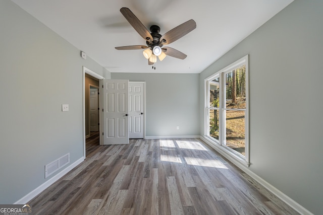 unfurnished bedroom with a ceiling fan, wood finished floors, visible vents, and baseboards