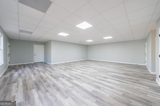 finished below grade area with visible vents, a drop ceiling, baseboards, and wood finished floors