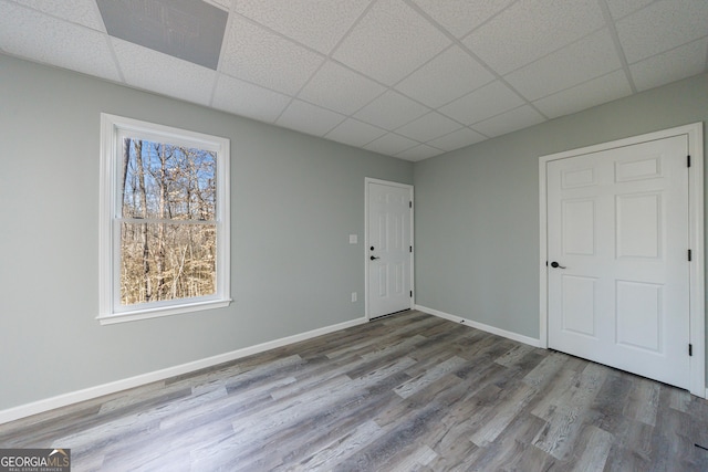 interior space with a drop ceiling, wood finished floors, visible vents, and baseboards