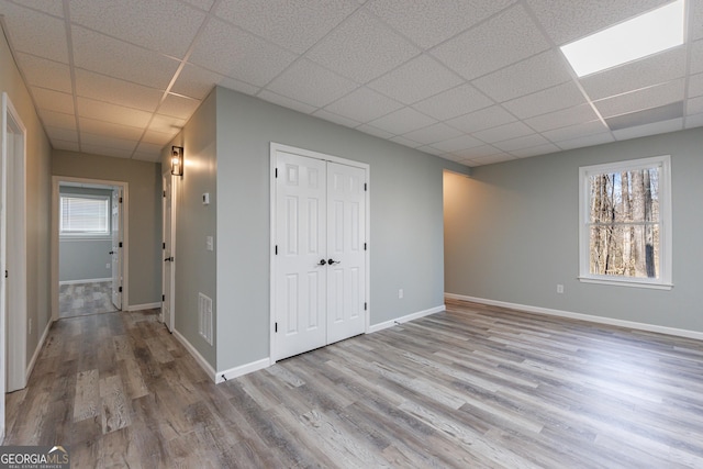 unfurnished bedroom with multiple windows, wood finished floors, a paneled ceiling, and baseboards