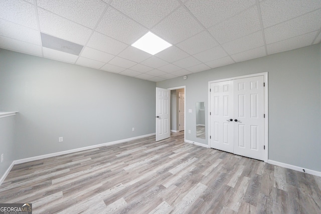 unfurnished bedroom with a closet, a drop ceiling, baseboards, and wood finished floors