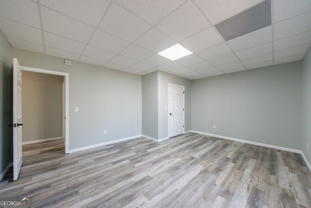 empty room featuring wood finished floors, a paneled ceiling, and baseboards